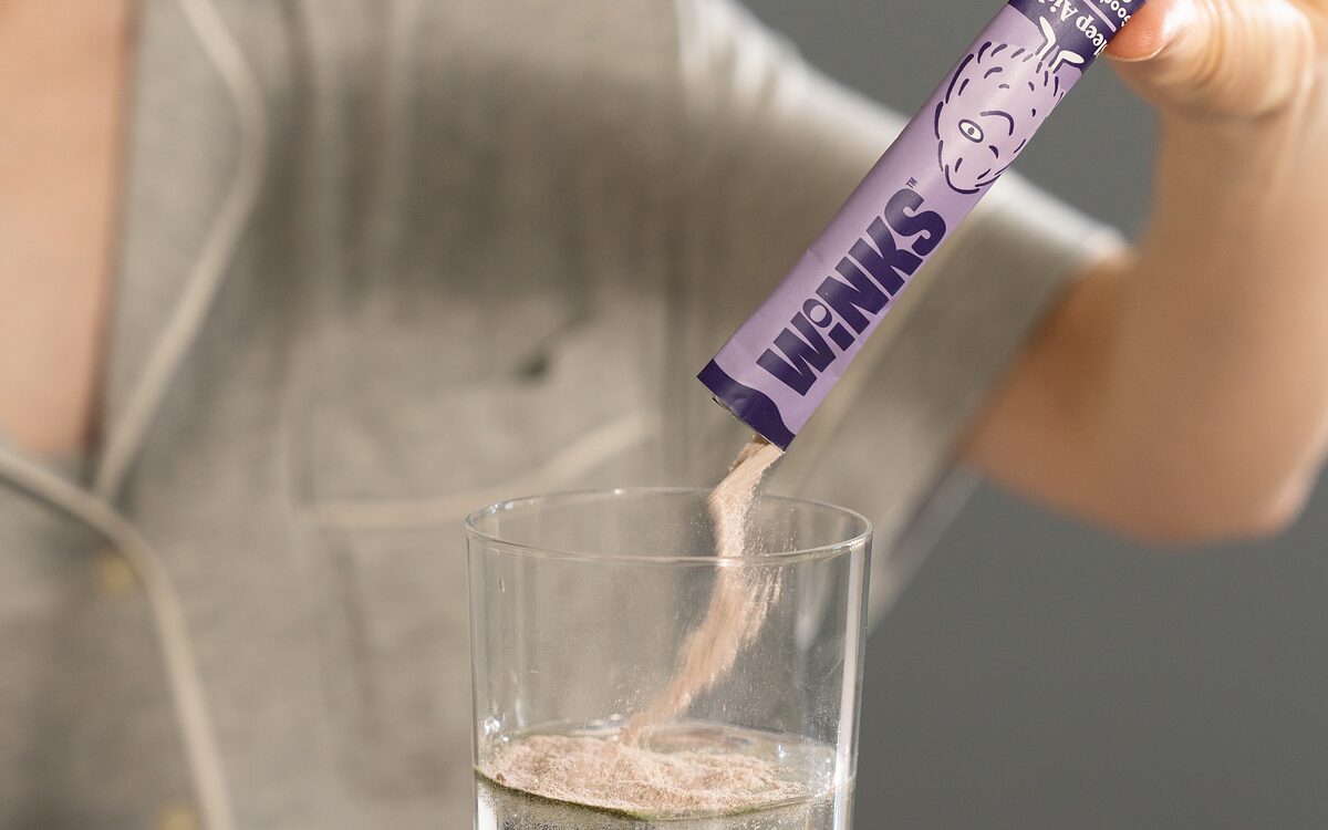 A hand tipping a Winks stick pack into a glass of cold water