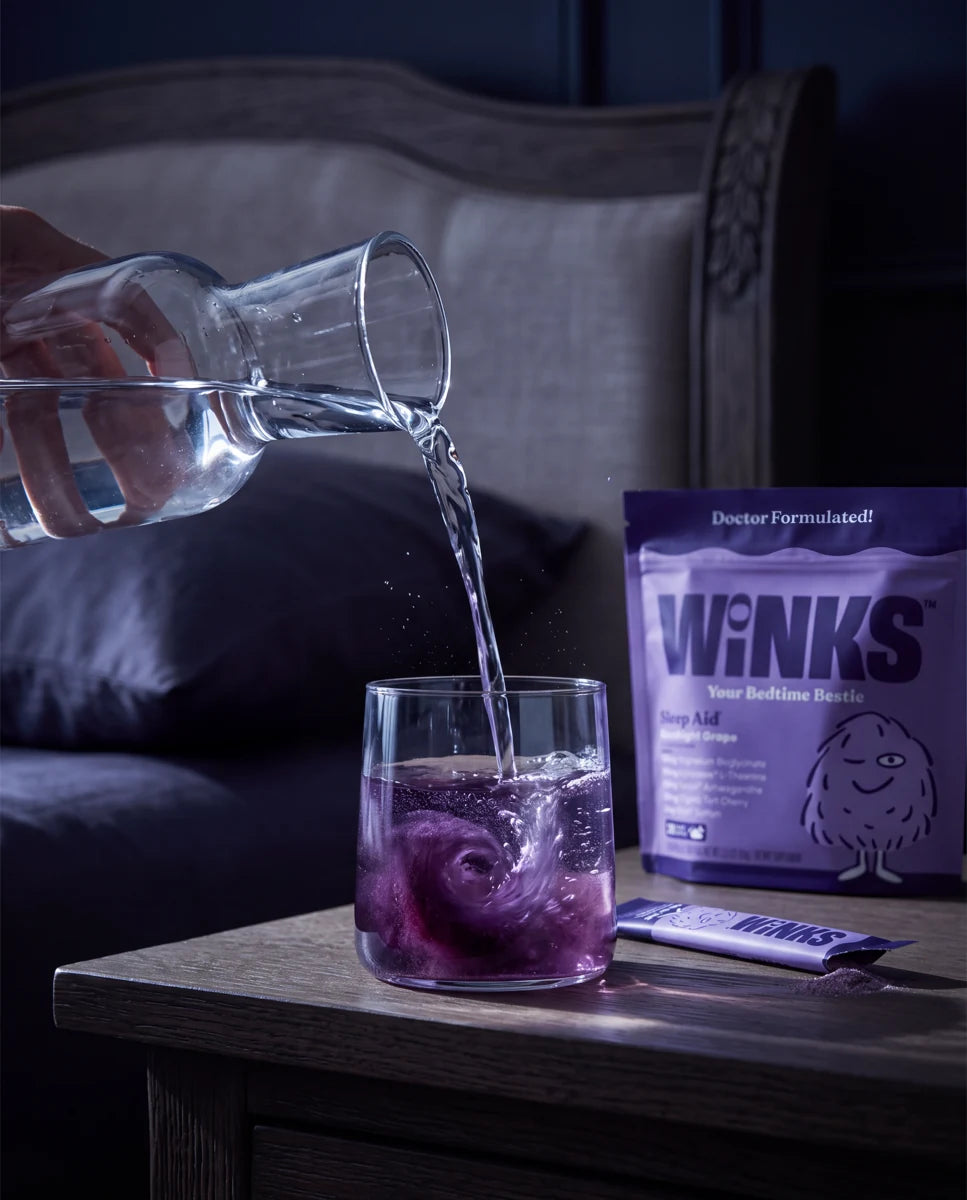 Water being poured into a small glass beside a Winks pouch and stick.