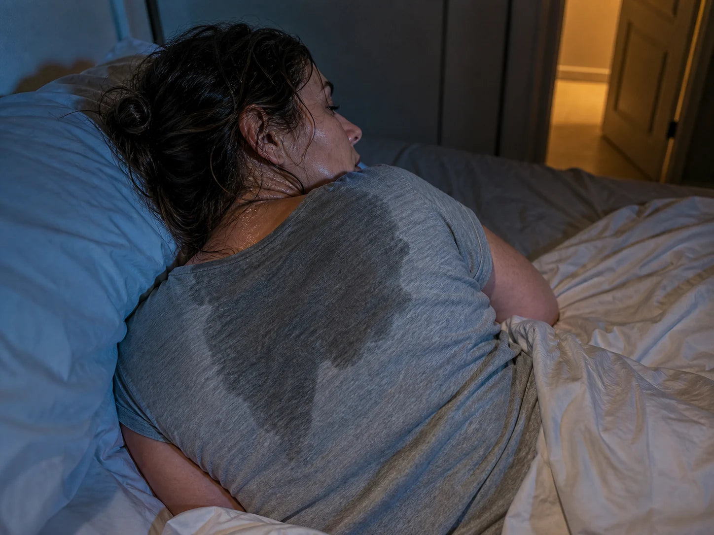 A woman in bed at night with visible sweat on her back and damp hair
