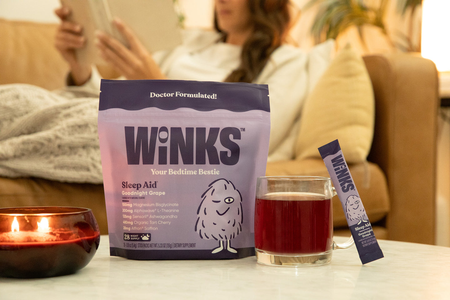 A Winks pouch and stick pack beside a filled glass on a table in warm evening lamplight