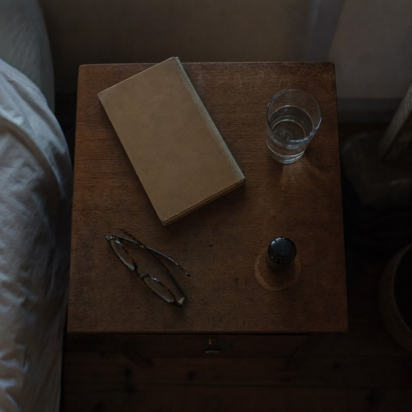 A bedside table at night, a bottle sitting where it always sits