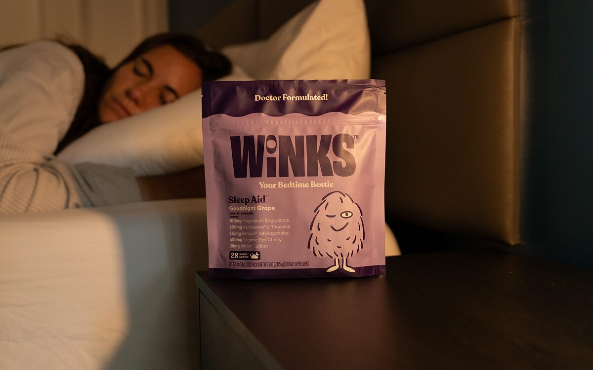 A Goodnight Grape pouch on a nightstand beside a sleeping woman
