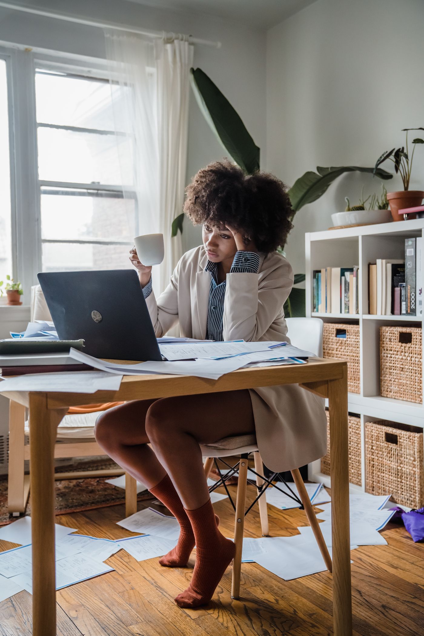 A woman holding coffee with her head resting in her hand beside a laptop