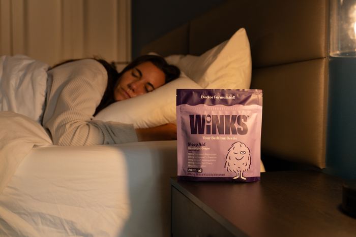 Winks studio photograph of a woman asleep beside her bedside table