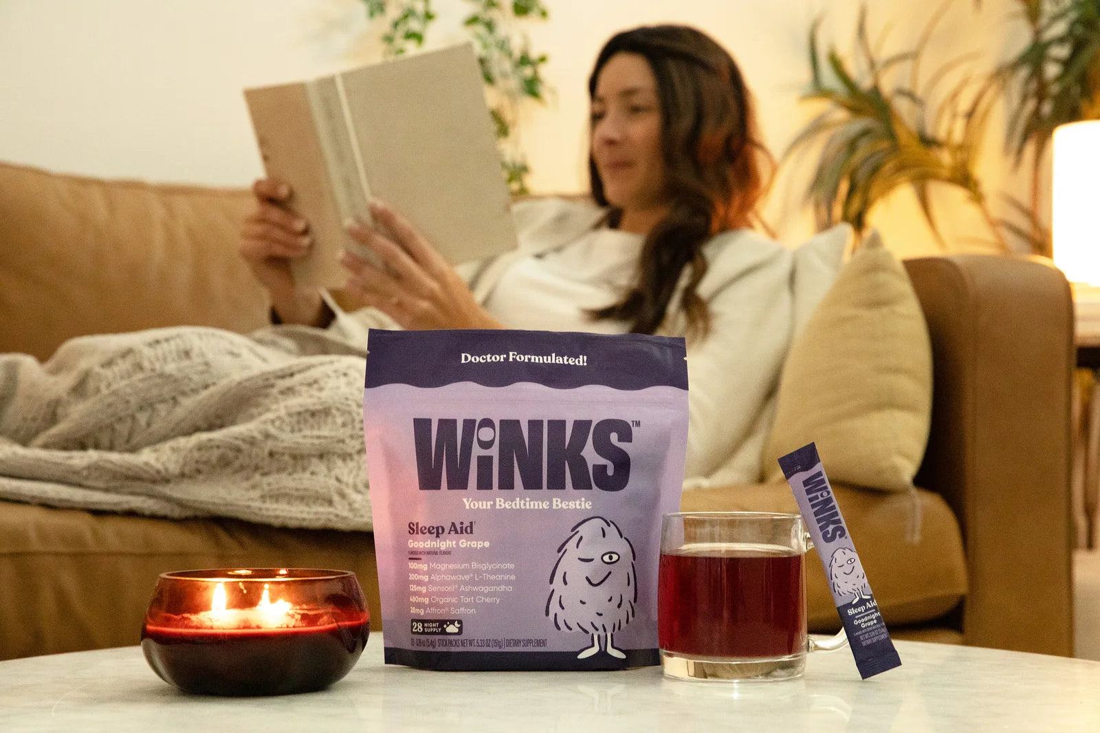 A woman reading on the couch beside a prepared glass of Winks as part of a bedtime routine